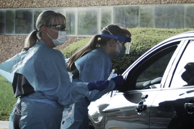 Nurses in protective gear administering a test to a patient in their car