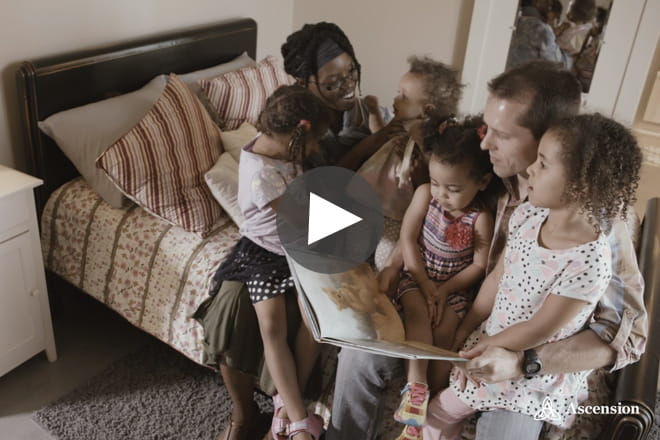 Young family reading a book. Video sharing Ascension patient stories. 