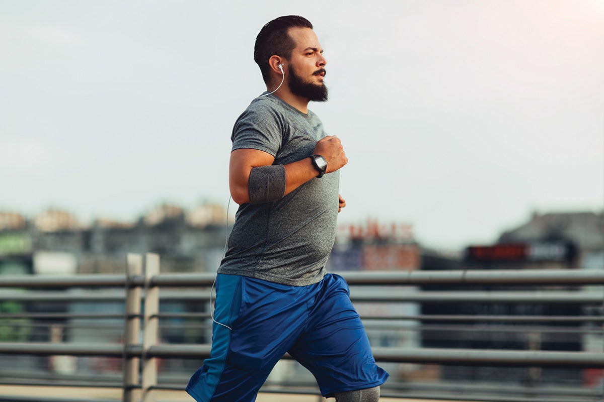 Man jogging outdoors on a city bridge wearing athletic gear and earbuds, promoting fitness and a healthy lifestyle.