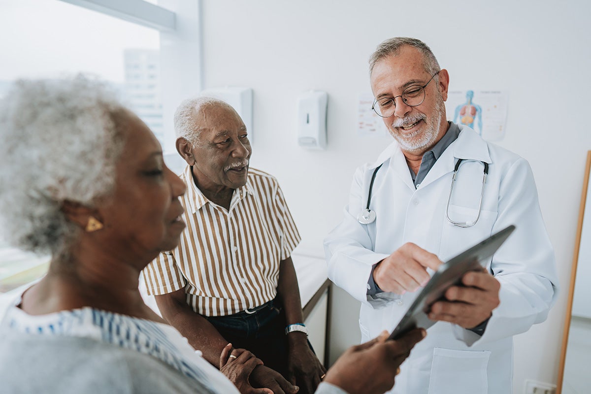 Doctor reviewing information on a tablet with two patients during a clinic visit.