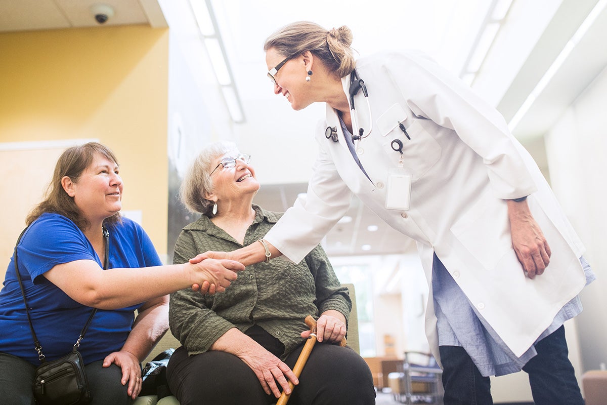 Doctor shaking hands with a patient while another patient sits beside her in a clinic waiting area.