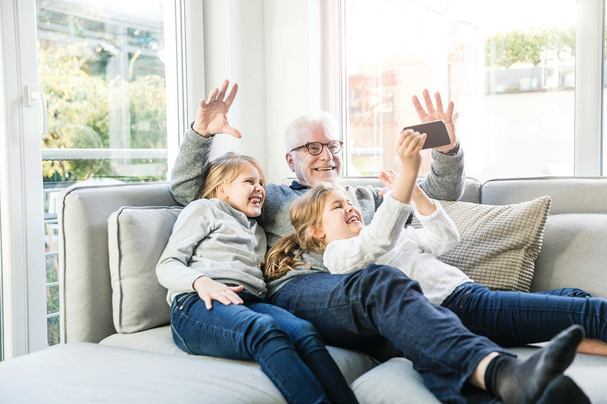 Grandfather and two children take a selfie together on a couch.