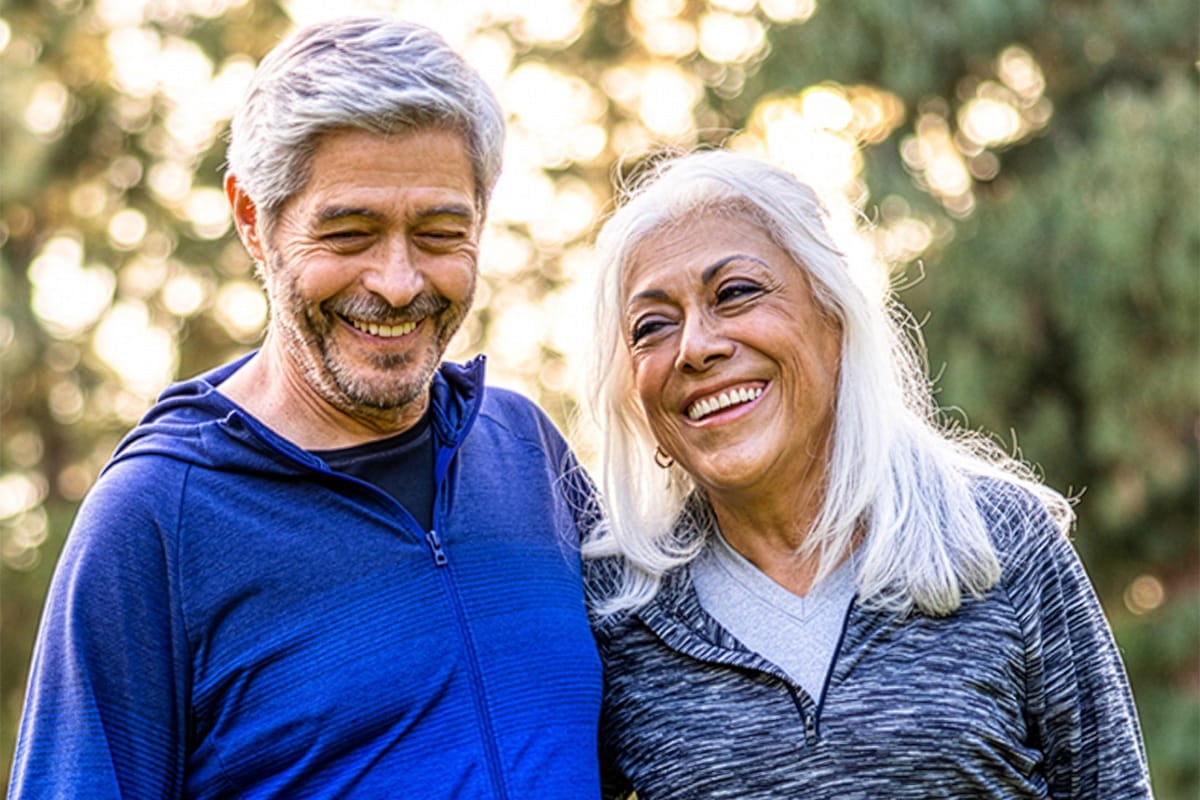 A smiling older couple standing close together outdoors, enjoying time in nature and sharing a happy moment.