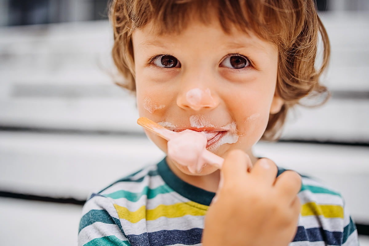 Young child with a messy face eating ice cream from a spoon, enjoying a sweet summer treat.
