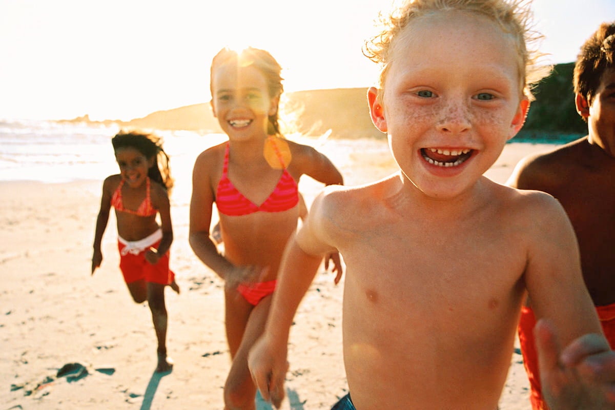 Group of children running and smiling on a sunny beach at sunset, promoting active summer fun and healthy outdoor play.