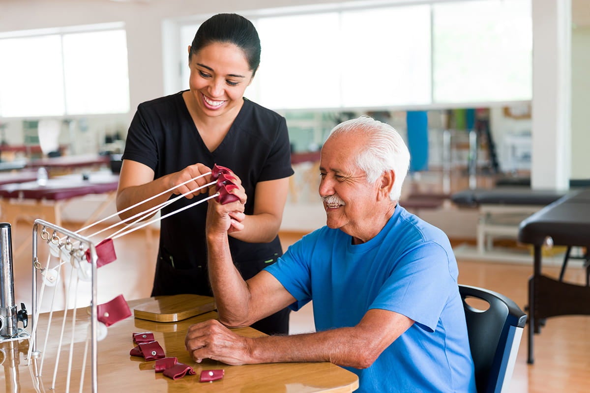 Therapist guiding an older adult through hand exercise using resistance bands during rehabilitation.