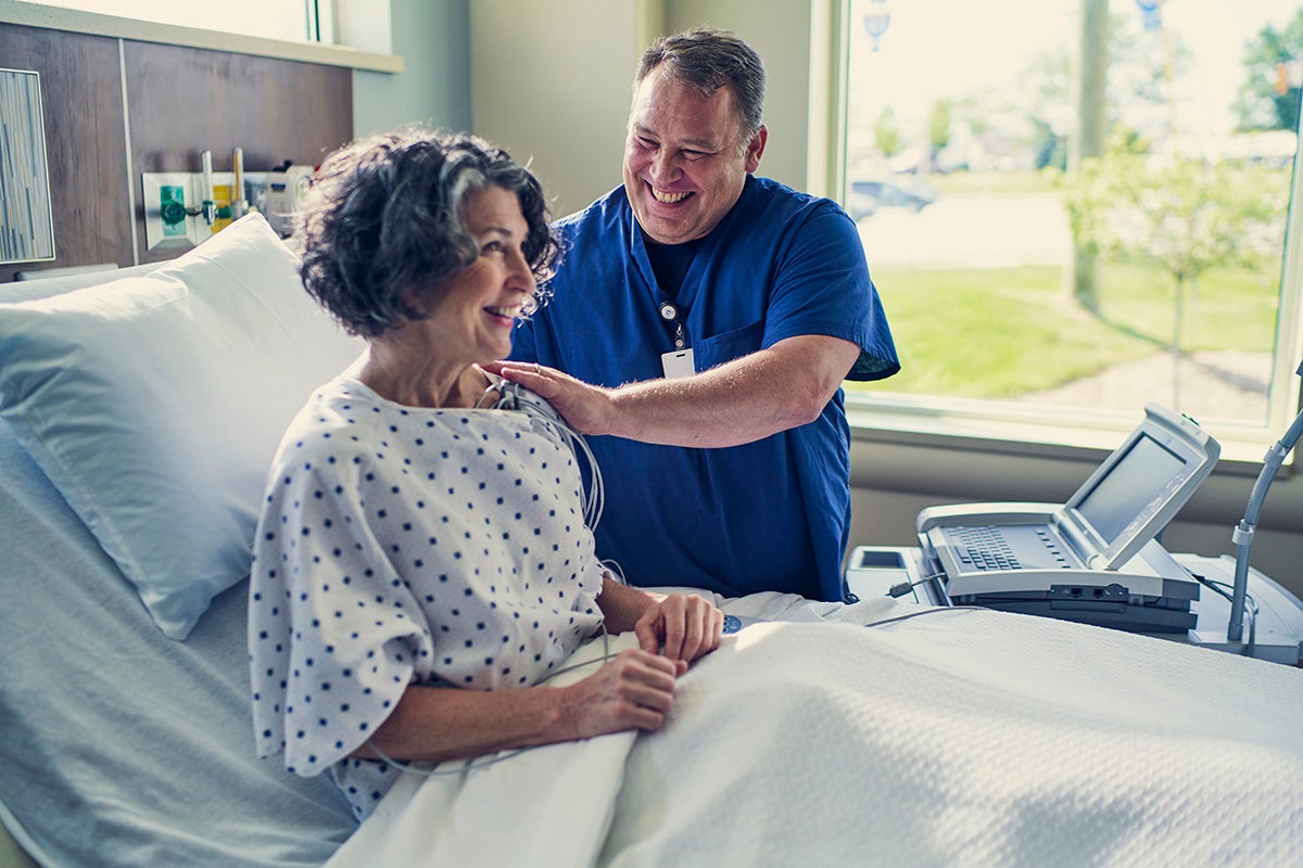 Nurse placing monitoring leads on a patient in a hospital bed during care.