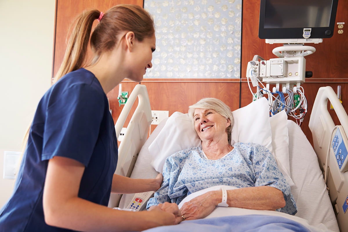 Nurse speaking with a patient resting in a hospital bed.