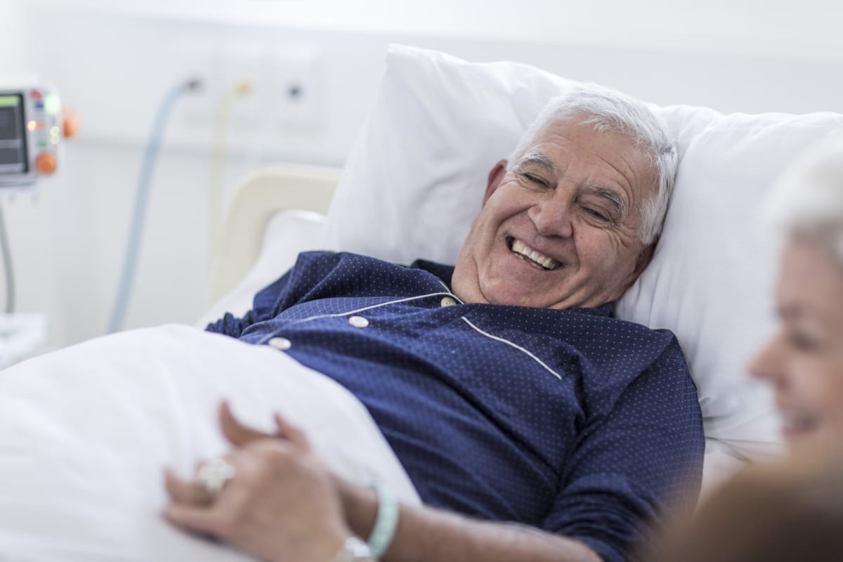 male patient in hospital bed smiling with family