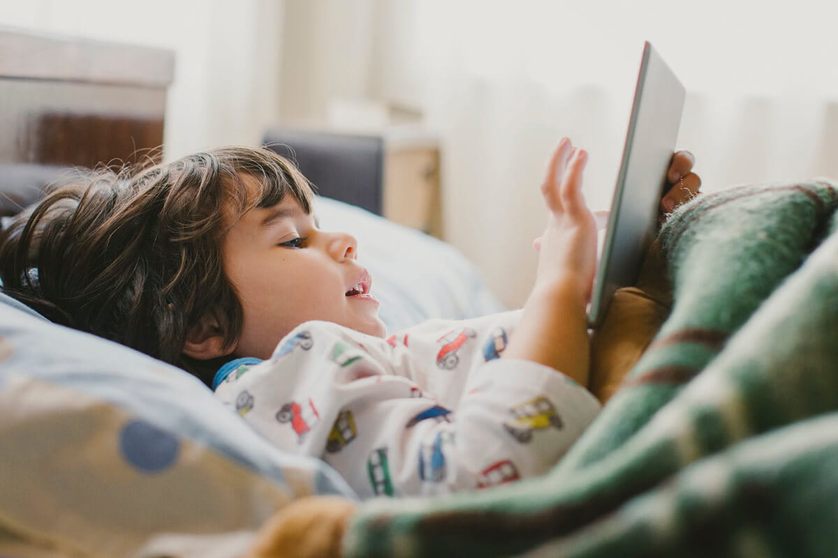 Child in bed playing on a tablet.