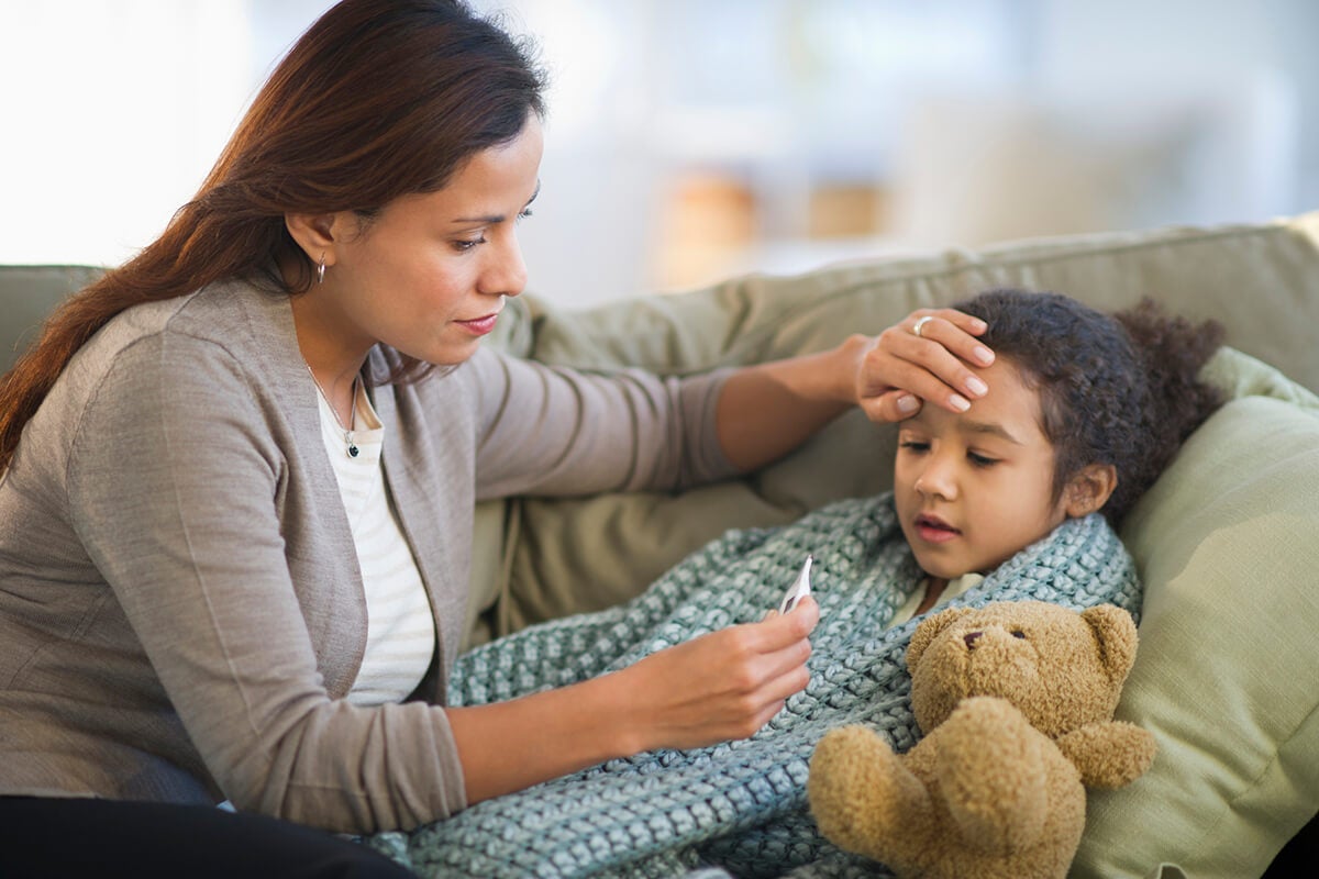 A mom checking the temperature of her child, to help make a decision on what type of care the child needs.