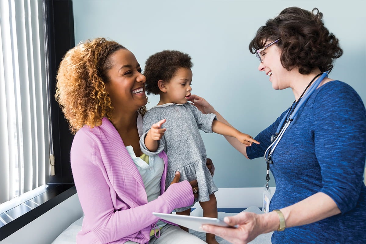 Provider examining a toddler while speaking with their mother during a clinic visit.