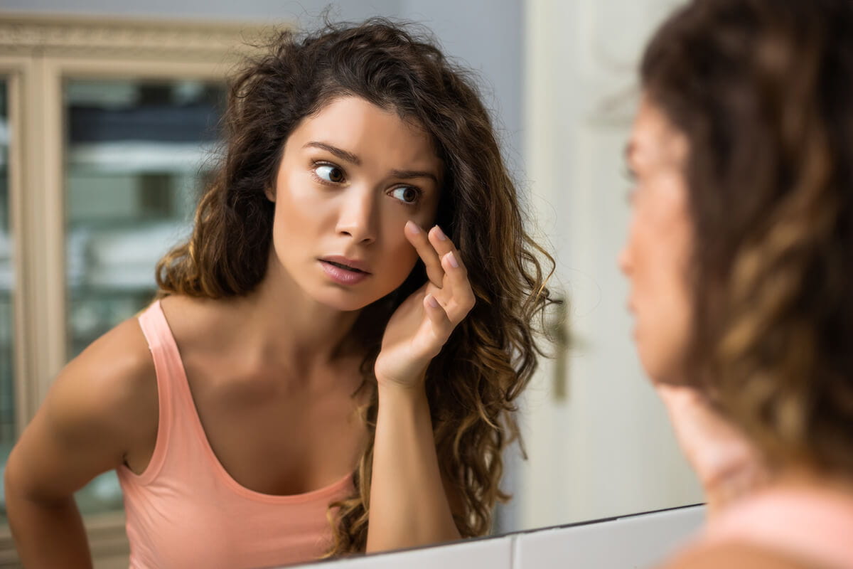 Woman looking at her skin in the mirror.