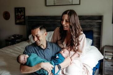 Lauren and Stefen sit with their twin boys on a bed