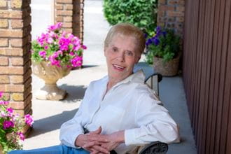 Joanne Owen in white shirt sitting down with pink flowers in background