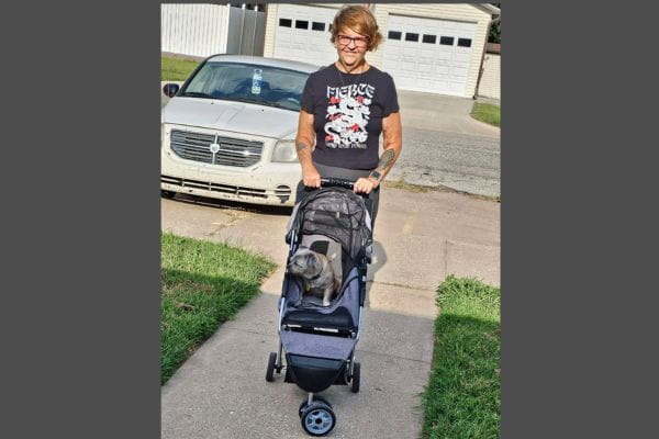 Melody outdoors with her dog, Venus, ready for a walk in a stroller