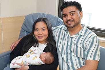 In a hospital room, a man and a woman cradle their baby, capturing a tender moment of new parenthood.