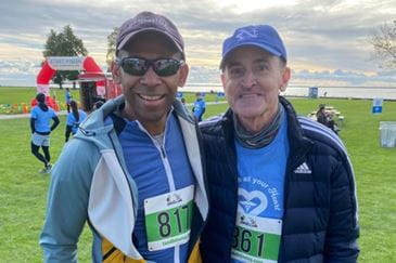 Two men stand together sporting jackets and bib numbers before a 5k race. (Dr. Burnett and Steve Olson).