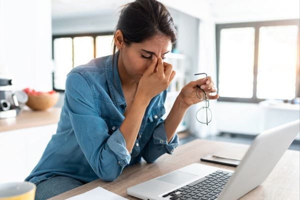 A woman sitting at a desk, rubbing her nose and looking stressed
