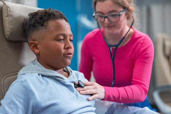 Healthcare provider listens to young boy’s chest with stethoscope in a pediatric emergency department.