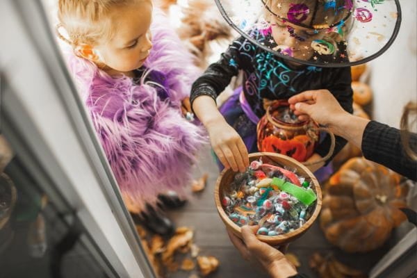 Two trick or treaters receive candy from an adult