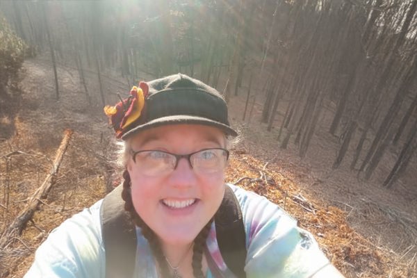 A middle aged woman takes a selfie in the woods during a fall hike.