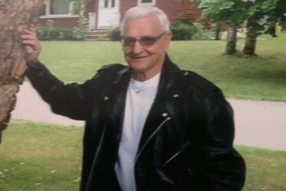 An elderly man poses for a photo in a leather jacket