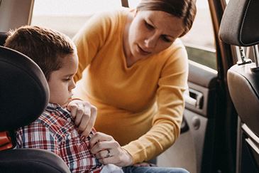 Adult securing a young child in a forward-facing car seat by fastening the chest clip and harness straps inside the back seat of a vehicle.