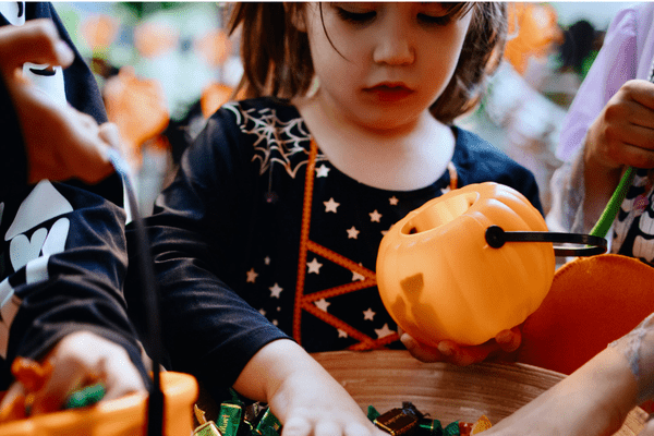 A child dressed in costume grabbing a handful of candy during trick or treating.