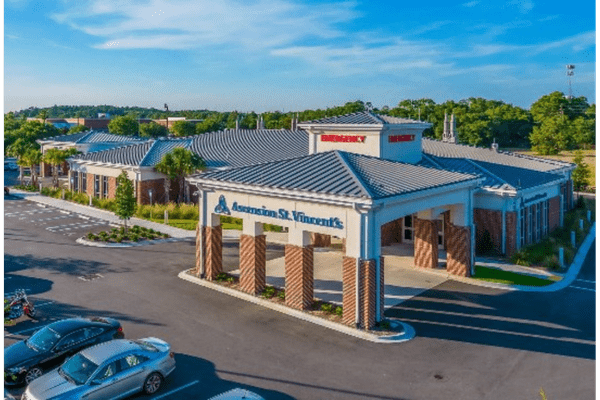 Exterior view of Ascension St. Vincent’s Emergency Care – Arlington, featuring a covered entrance with brick columns, emergency signage, and a parking lot in front of the building.