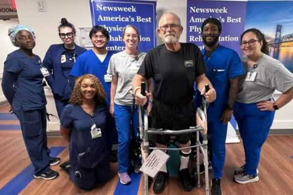 Mark stands with a walker surrounded by members of his rehabilitation care team.