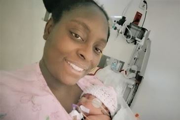 A smiling mother in a hospital bed gently holds her premature newborn, who is wearing a pink hat and connected to medical monitoring equipment, reflecting a high-risk pregnancy and NICU care journey during severe preeclampsia.