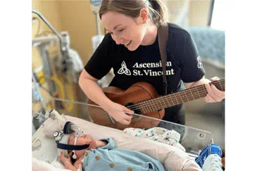 Jenny Kaufman plays the guitar and sings over a patient in a NICU crib.