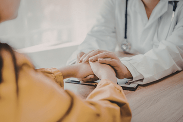A doctor  holding a patient’s hands during a discussion about cancer genetic testing services in Kansas.