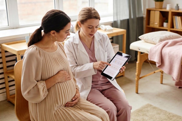 A young, pregnant woman evaluates her health information with her doctor.