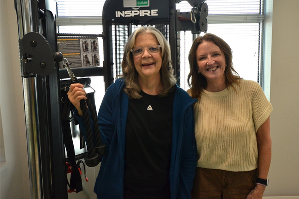 Risa Rehmert and fitness instructor Trish Gaston smile beside exercise equipment at the Ascension Via Christi Cancer Wellness Center.