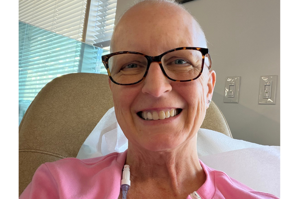 Amanda smiles wearing glasses and a pink top while seated in a medical treatment room.