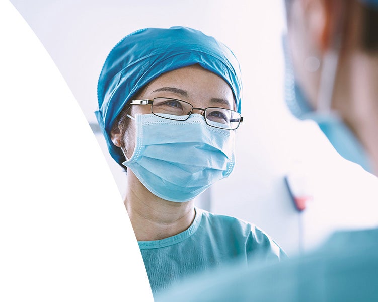 Surgeon wearing a mask and scrubs speaking with a colleague in a clinical setting.