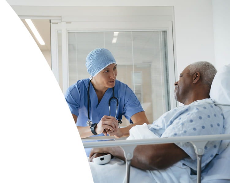 Provider holding a patient’s hand while speaking during a hospital stay.