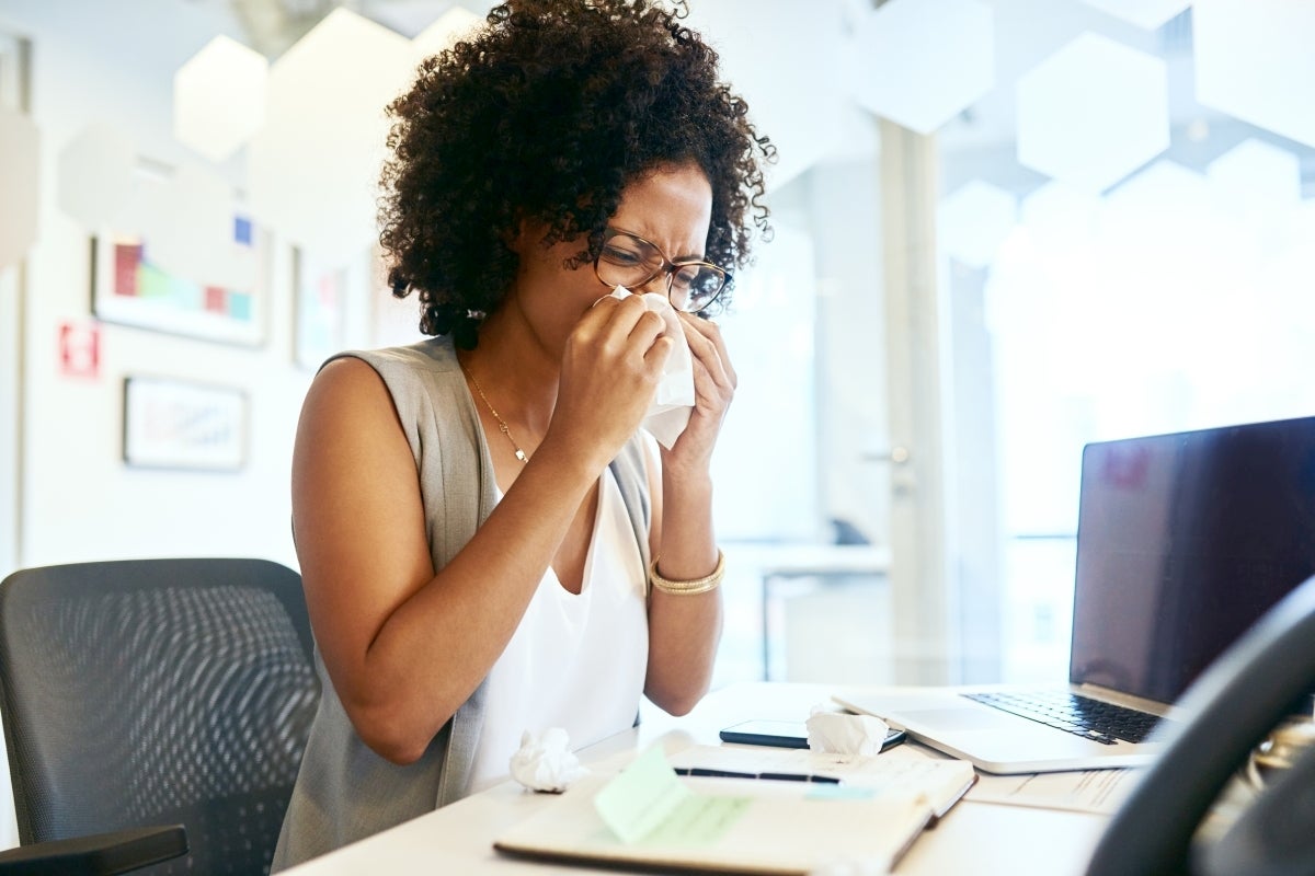 A woman blows her knows while working in front of her computer.