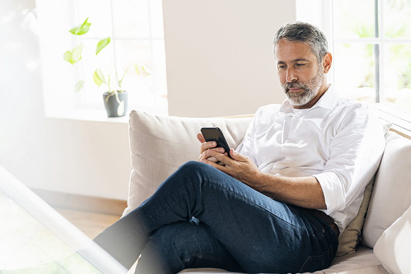 A man sitting relaxed on couch looking at smartphone.