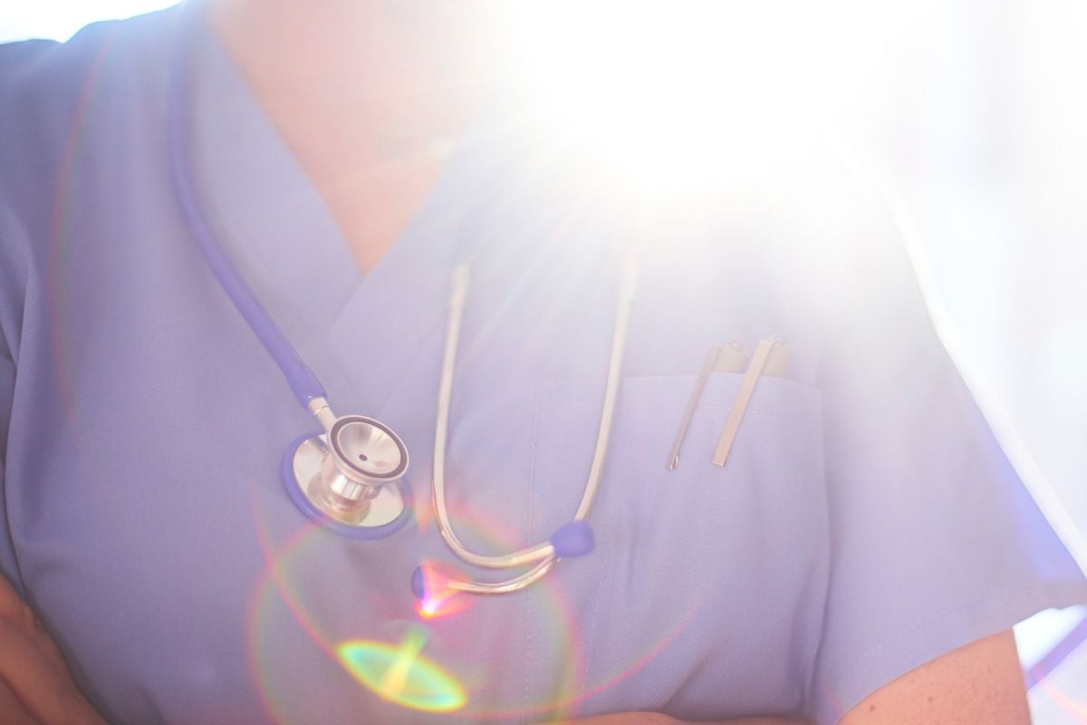 A healthcare provider wearing a stethoscope, standing in front of a window with sunlight pouring over their shoulder
