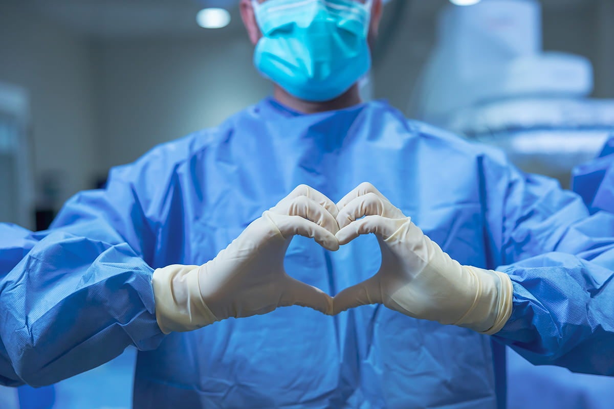 A surgeon forms the shape of a heart with his hands.