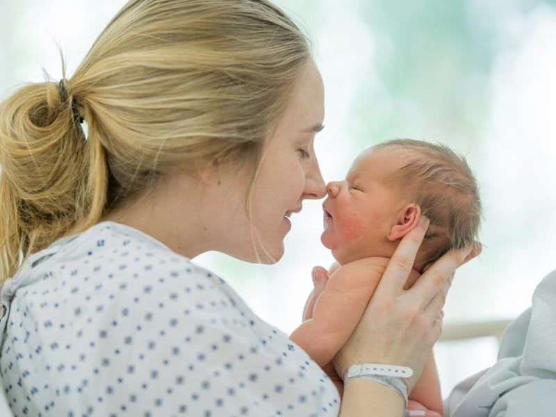 A mother in a hospital gown gently holds her newborn baby close as they touch noses, creating a tender bonding moment shortly after birth.