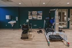 Physical therapy gym featuring body-weight support treadmill technology, recumbent exercise equipment, and open space for personalized rehabilitation sessions.