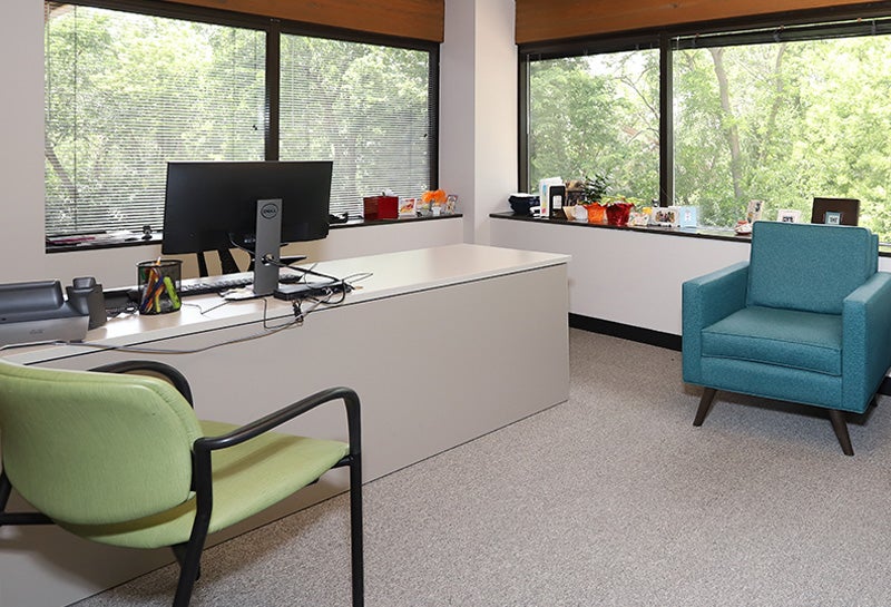Private office with desk, computer, and chairs near large windows with natural light.