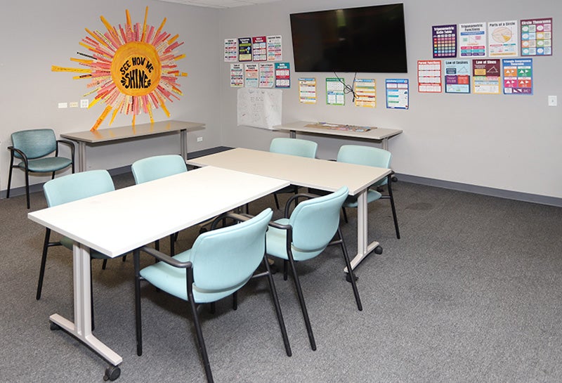 Group therapy room with tables, chairs, wall posters, and a display screen.