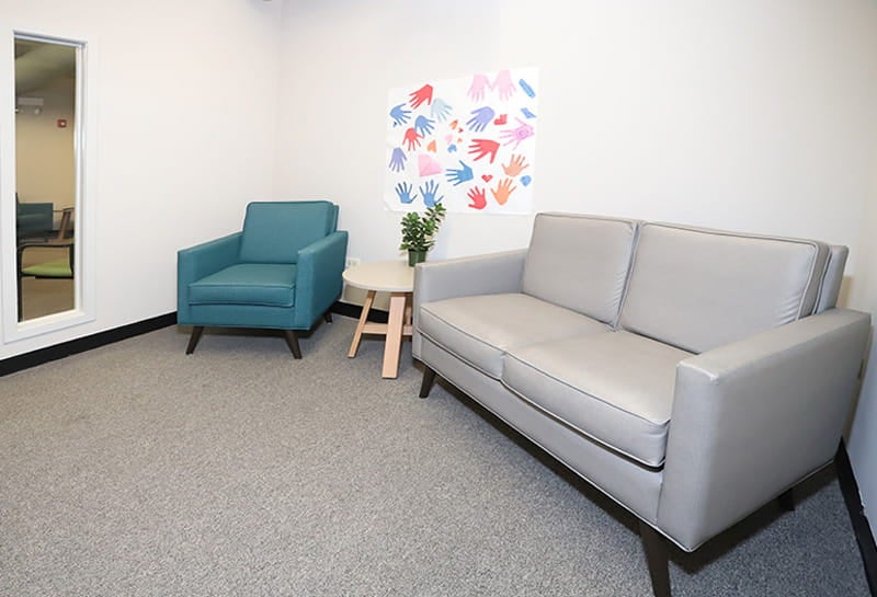 Waiting area with sofa, chair, small table, and wall art in a calm setting.