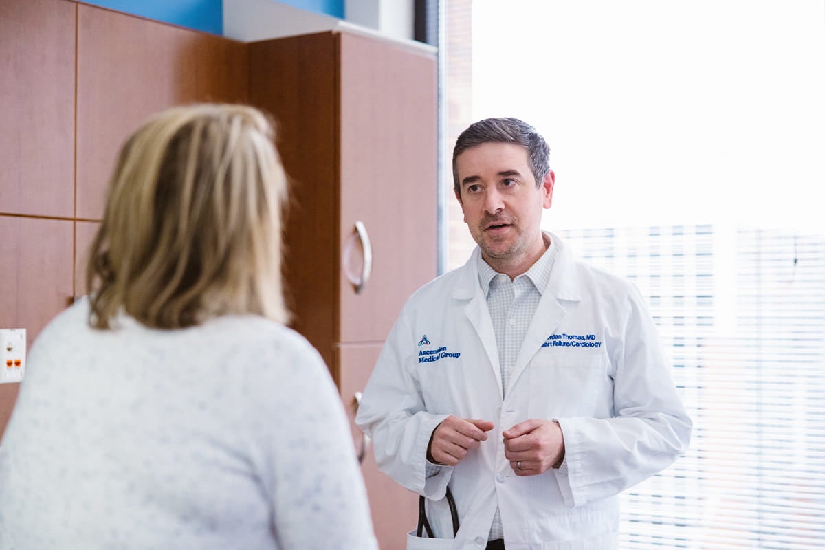 Doctor in a white coat speaks with a patient in a medical exam room.