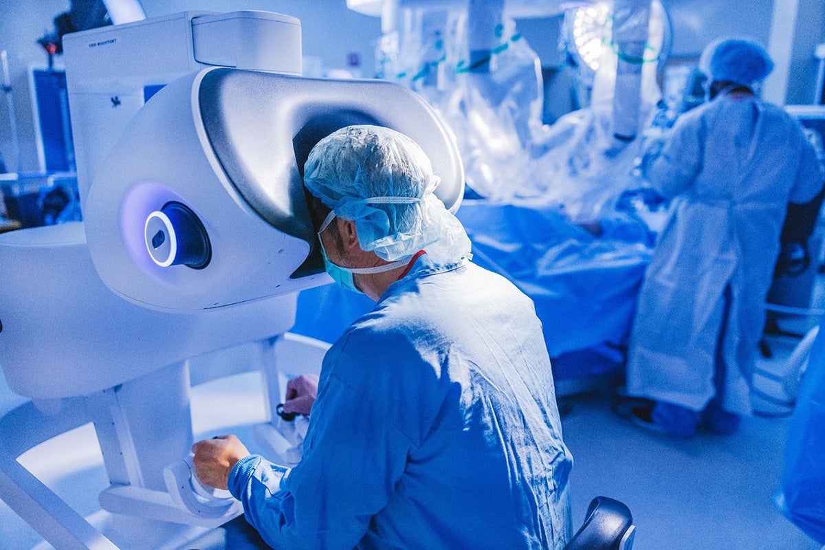 Clinician operating a robotic surgery console while surgical team works in background.